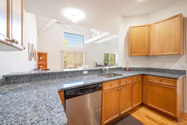 kitchen featuring stainless steel dishwasher, a sink, dark stone countertops, light wood-type flooring, and a ceiling fan