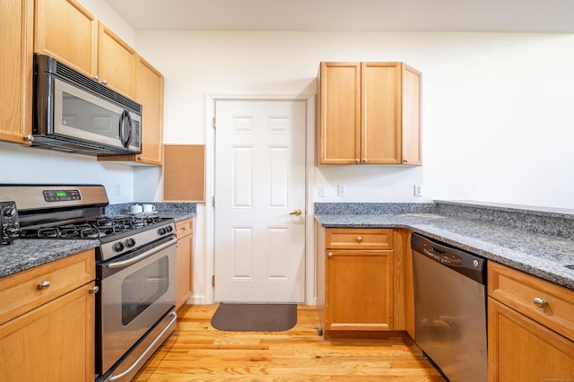 kitchen with appliances with stainless steel finishes, light wood-style floors, and dark stone countertops