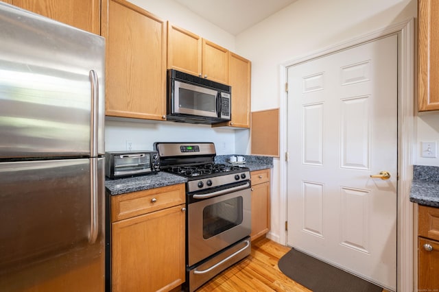 kitchen featuring stainless steel appliances, light wood finished floors, dark stone countertops, and light brown cabinetry