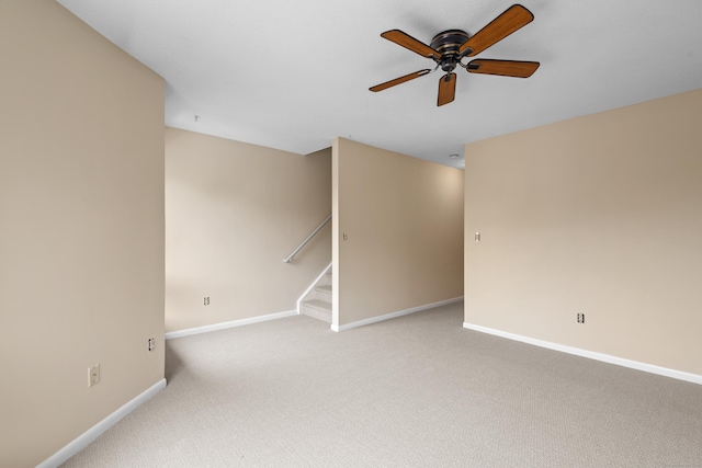 unfurnished room featuring baseboards, ceiling fan, light colored carpet, and stairway