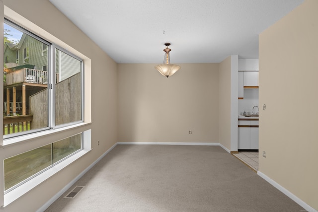 unfurnished room featuring light carpet, baseboards, and a sink