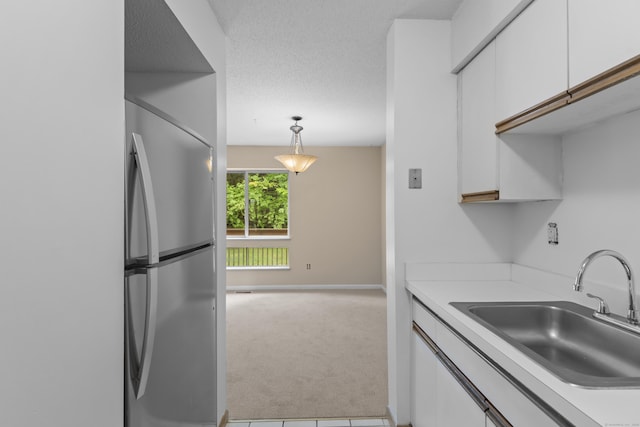 kitchen featuring freestanding refrigerator, a sink, light colored carpet, and white cabinets