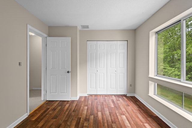 unfurnished bedroom with dark wood finished floors, a closet, and baseboards