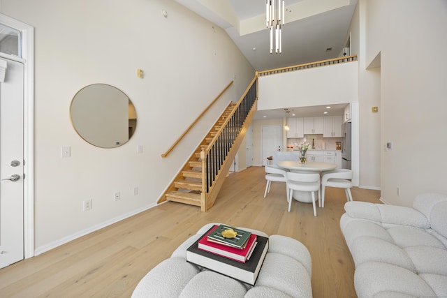 living room featuring stairway, a towering ceiling, light wood finished floors, baseboards, and recessed lighting