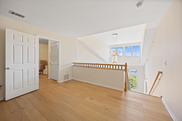 empty room with light wood finished floors, baseboards, a chandelier, and a smoke detector