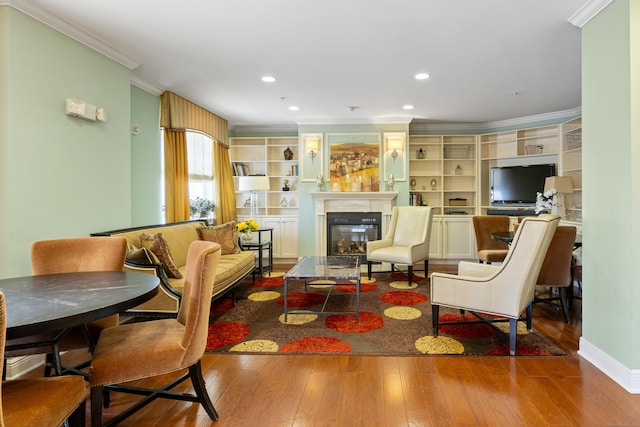 living area with ornamental molding, wood finished floors, a glass covered fireplace, recessed lighting, and baseboards
