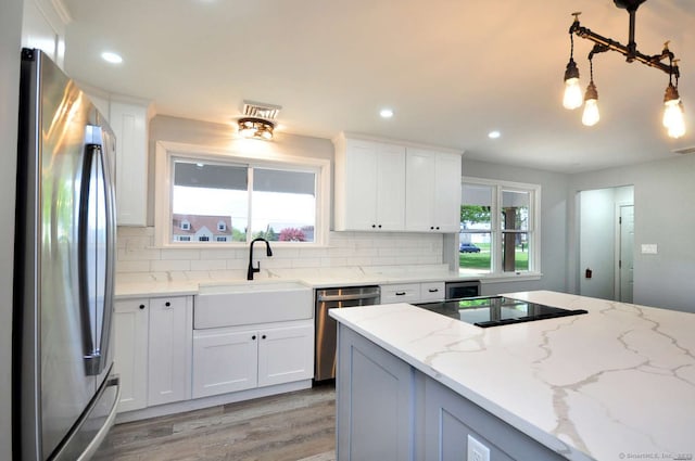 kitchen with stainless steel appliances, a sink, light wood-style floors, tasteful backsplash, and white cabinetry