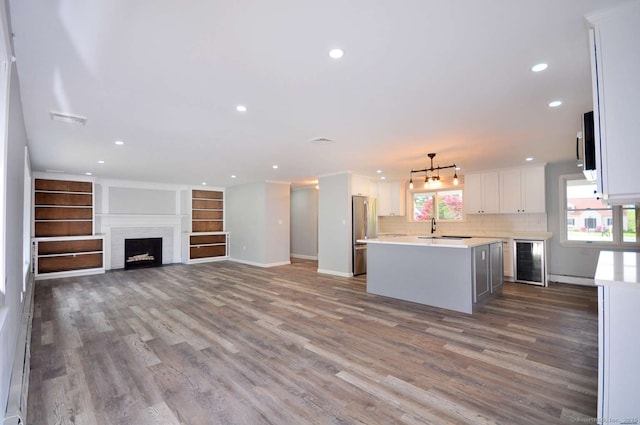 kitchen with beverage cooler, a sink, light countertops, wood finished floors, and a center island