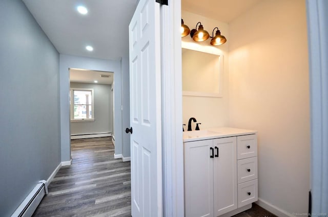 corridor with a baseboard radiator, a sink, dark wood-style flooring, baseboards, and recessed lighting