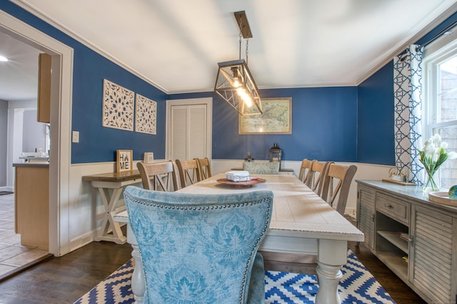 dining space featuring dark wood-type flooring, crown molding, and a wainscoted wall