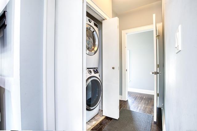 laundry room featuring stacked washer / drying machine, dark wood-type flooring, and baseboards