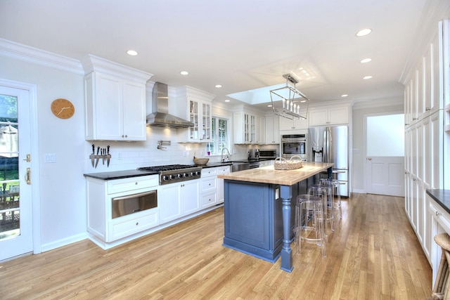81 Grumman Hill Rd, Wilton, CT 06897 - kitchen featuring wall chimney range hood, appliances with stainless steel finishes, a warming drawer, light wood finished floors, and white cabinetry