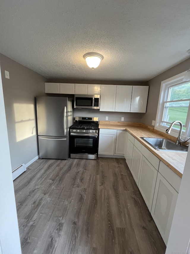 kitchen with appliances with stainless steel finishes, a sink, a baseboard heating unit, dark wood finished floors, and white cabinets