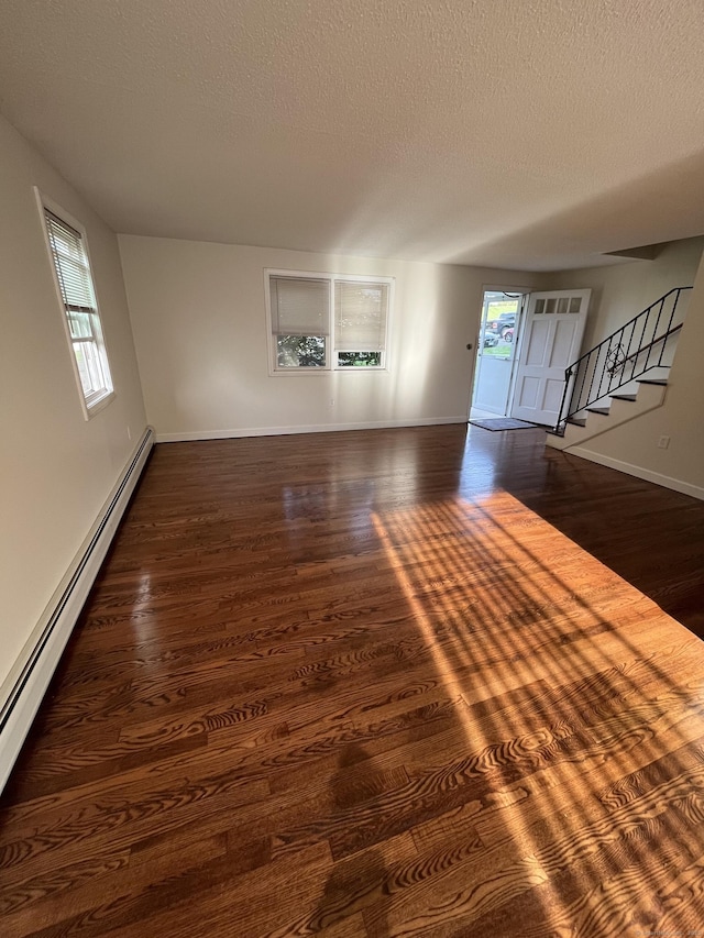 unfurnished living room with a baseboard heating unit, plenty of natural light, wood finished floors, baseboards, and a textured ceiling