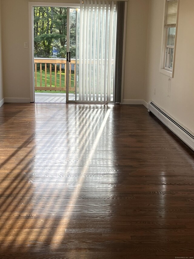 unfurnished room featuring baseboards, dark wood-type flooring, and a baseboard heating unit