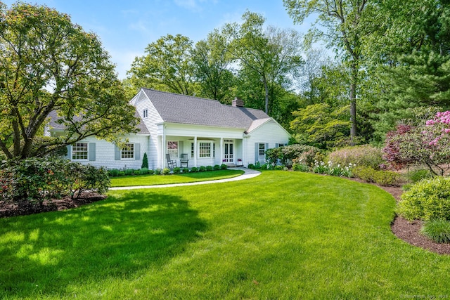 view of front of home featuring a chimney, a front yard, covered porch, and a shingled roof