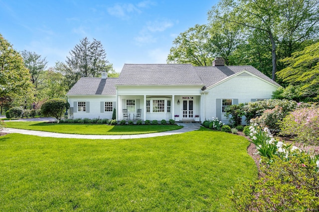 view of front of house featuring a chimney, a front lawn, a porch, and a shingled roof