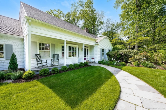 bungalow featuring covered porch, a front yard, a chimney, and roof with shingles