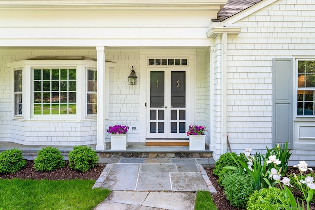 entrance to property with a porch and a shingled roof