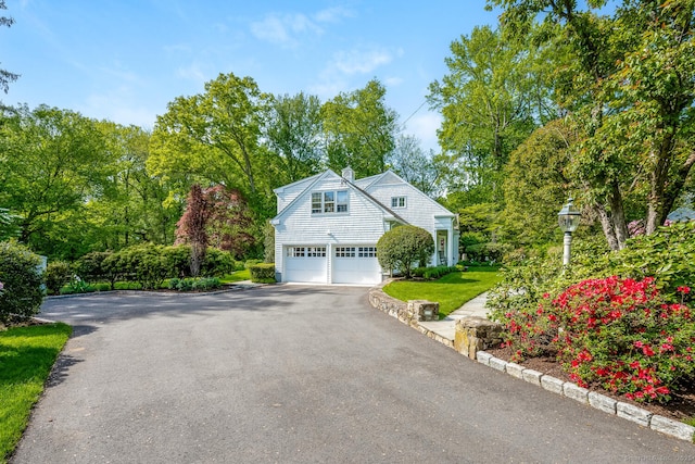 view of side of home featuring asphalt driveway, a chimney, a garage, and a lawn