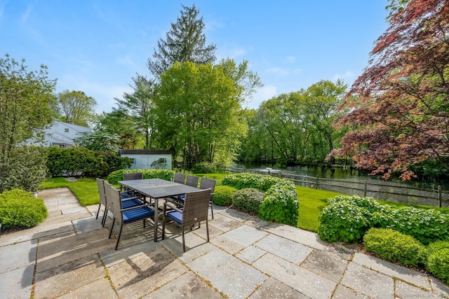 view of patio featuring outdoor dining space, a water view, and an outbuilding