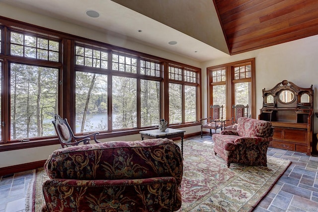 living room with healthy amount of natural light, stone tile floors, vaulted ceiling, baseboards, and a water view