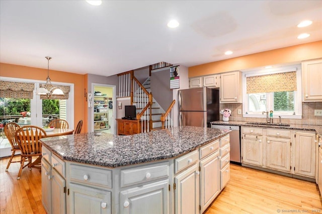kitchen with stainless steel appliances, a sink, a center island, light wood-type flooring, and dark stone counters