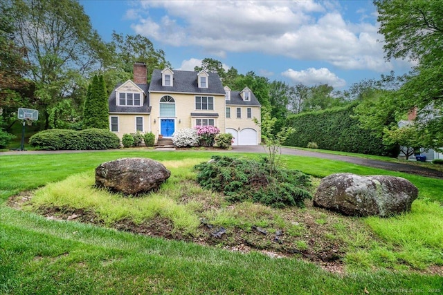 view of front of house with driveway, an attached garage, a chimney, and a front yard