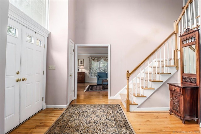 entrance foyer featuring stairs, a towering ceiling, wood finished floors, and baseboards