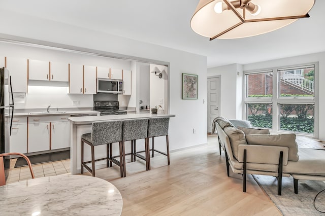 42 Temple Ct Unit 42, New Haven, CT 06511 - kitchen with stainless steel microwave, black / electric stove, a sink, a breakfast bar area, and white cabinets