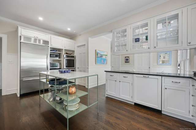 kitchen featuring built in appliances, white cabinetry, ornamental molding, glass insert cabinets, and dark wood-type flooring