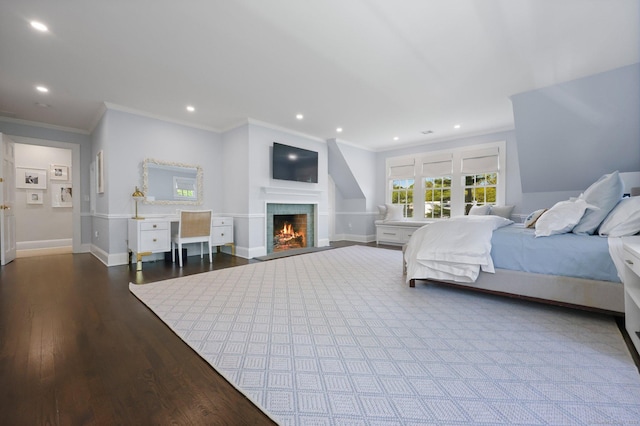 bedroom with crown molding, wood finished floors, baseboards, a warm lit fireplace, and recessed lighting