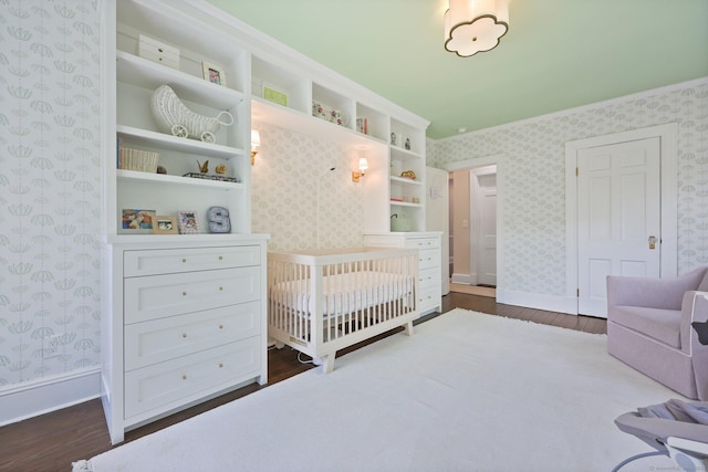 bedroom with wallpapered walls, dark wood-style floors, baseboards, and a nursery area
