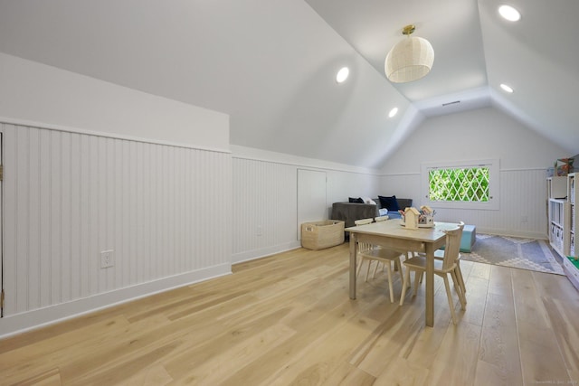 dining area featuring light wood finished floors, wainscoting, lofted ceiling, and a decorative wall