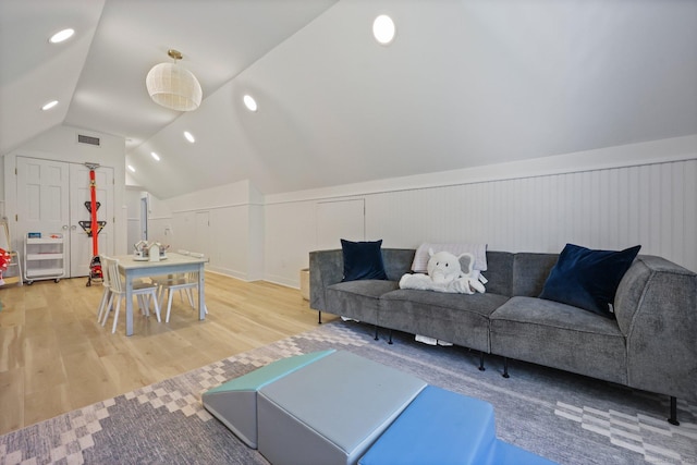 living room featuring light wood-type flooring, lofted ceiling, and a wainscoted wall