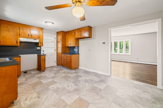 kitchen featuring a baseboard radiator, brown cabinets, under cabinet range hood, baseboards, and a ceiling fan