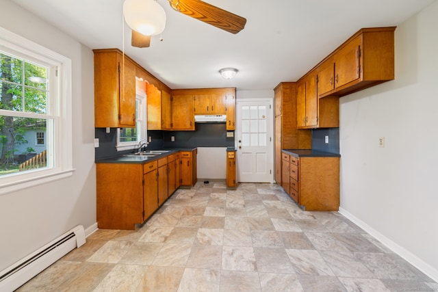 kitchen featuring a baseboard radiator, brown cabinetry, under cabinet range hood, and healthy amount of natural light