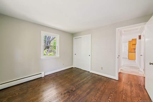 unfurnished bedroom featuring baseboard heating, wood finished floors, baseboards, and a closet