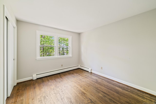 unfurnished bedroom featuring a baseboard heating unit, baseboards, wood finished floors, and a closet