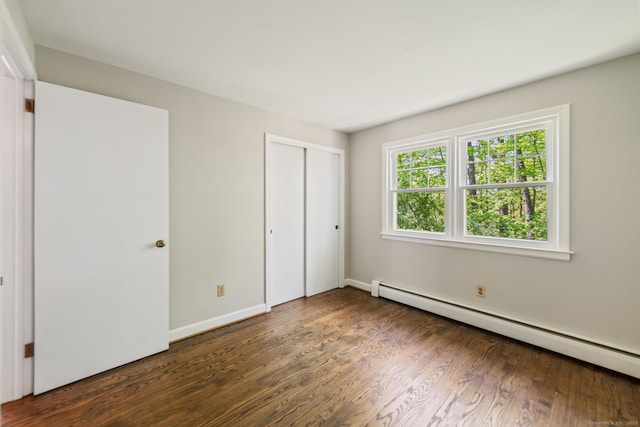 unfurnished bedroom featuring a baseboard heating unit, wood finished floors, a closet, and baseboards