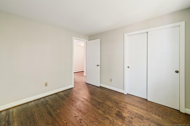 unfurnished bedroom featuring a baseboard radiator, baseboards, dark wood-style flooring, and a closet
