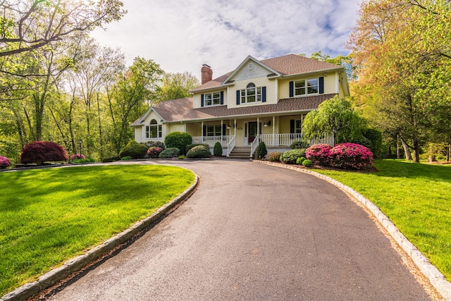 view of front facade featuring a porch, a chimney, driveway, and a front lawn