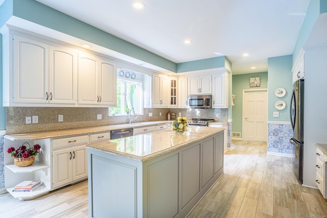 kitchen with stainless steel appliances, light wood finished floors, light stone counters, white cabinets, and recessed lighting