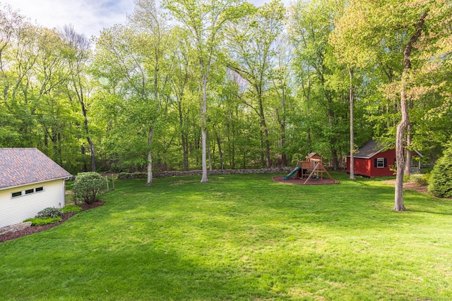 view of green lawn featuring a playground and an outbuilding