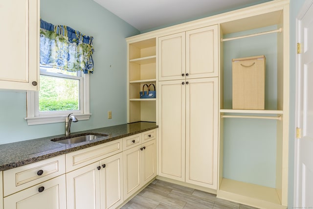 kitchen featuring a sink, cream cabinets, open shelves, and dark stone counters