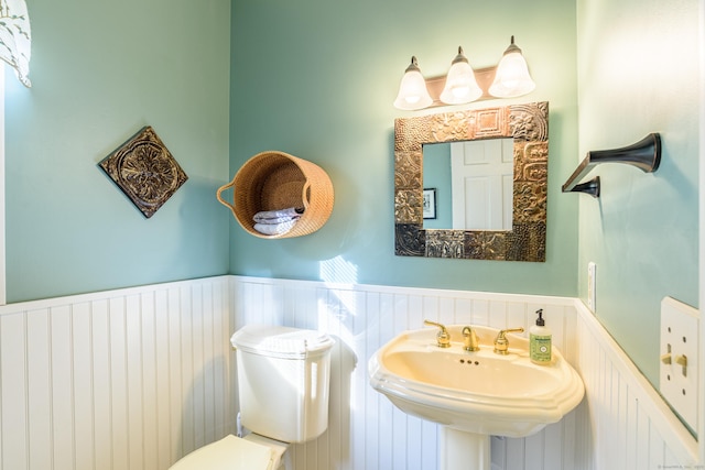 bathroom featuring a wainscoted wall, a sink, a decorative wall, and toilet