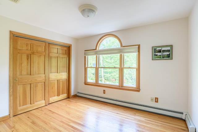 unfurnished bedroom with baseboard heating, light wood-style flooring, and a closet