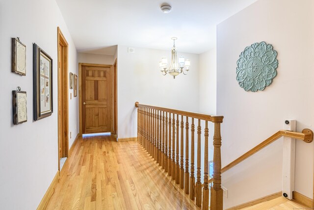 hall featuring an upstairs landing, light wood-style flooring, a chandelier, and baseboards