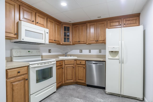 kitchen with white appliances, a sink, brown cabinets, light countertops, and glass insert cabinets