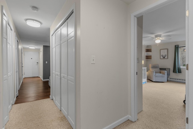 hallway with a baseboard radiator, light colored carpet, and baseboards